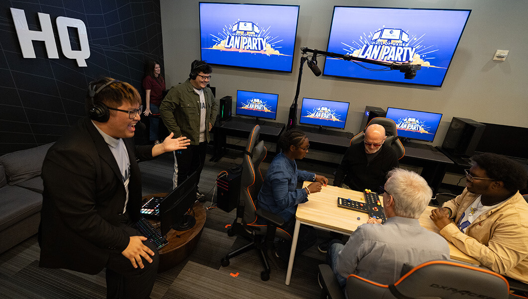 Garry Jones y Jon Phelps se sientan frente a un juego de mesa con dos estudiantes mientras otros estudiantes están cerca y observan.